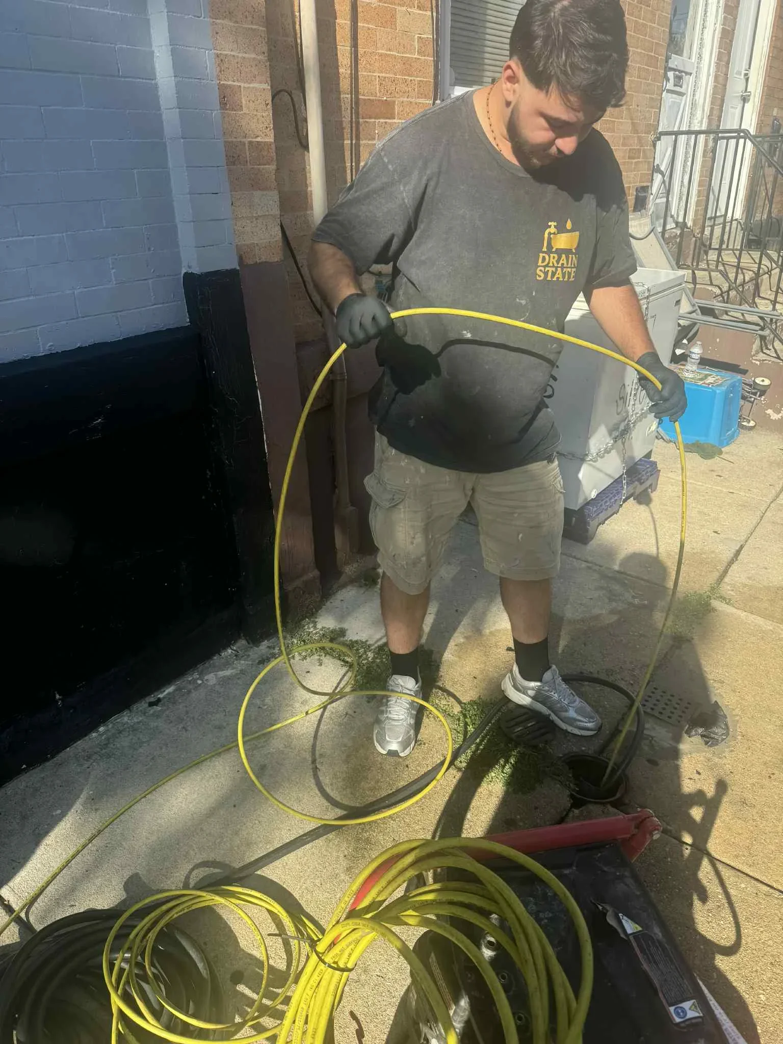 Technician operating high-pressure drain cleaning equipment with yellow hoses on residential concrete pad