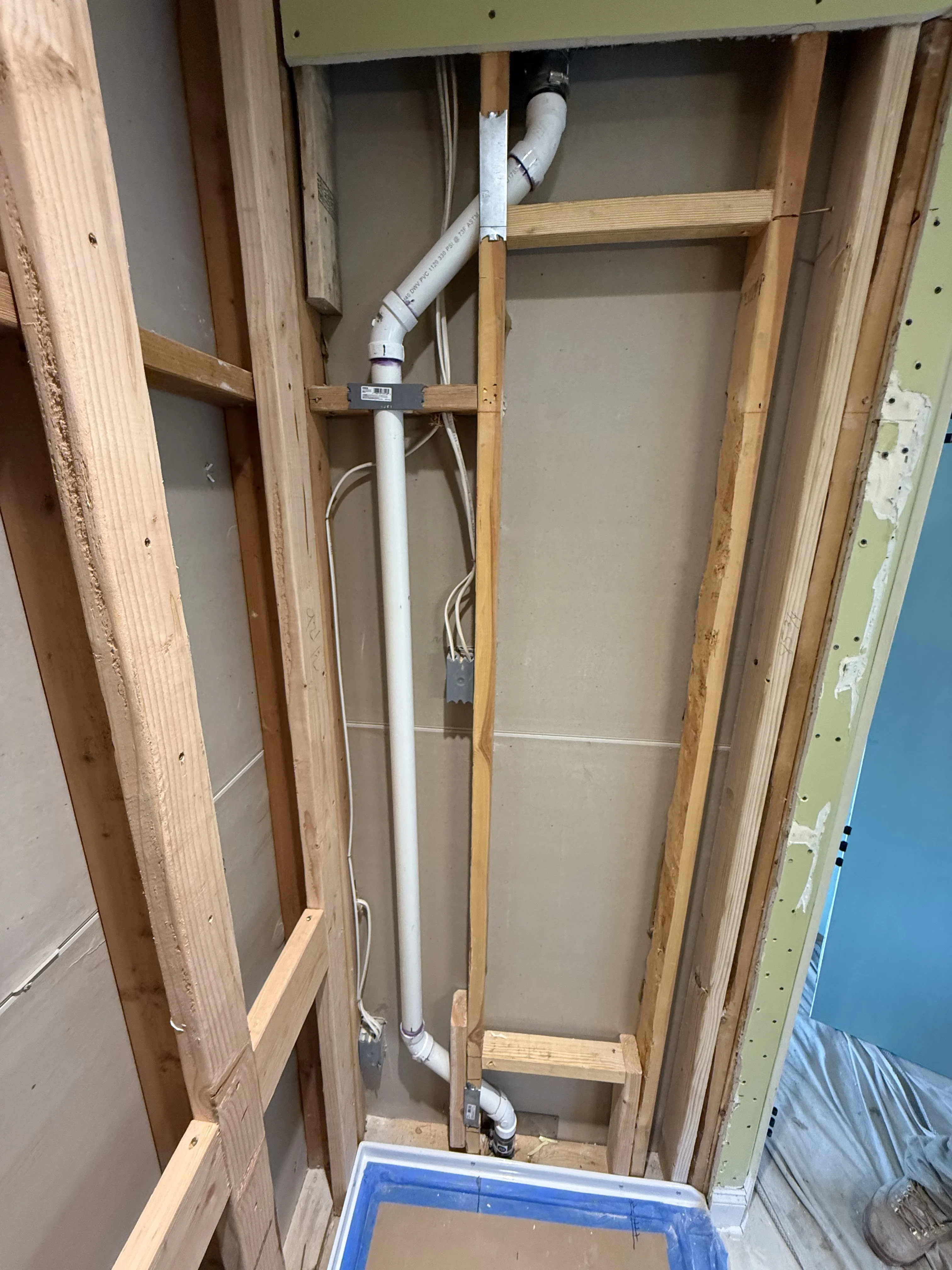 White PVC drain pipe installation with wooden framing and support brackets in wall cavity
