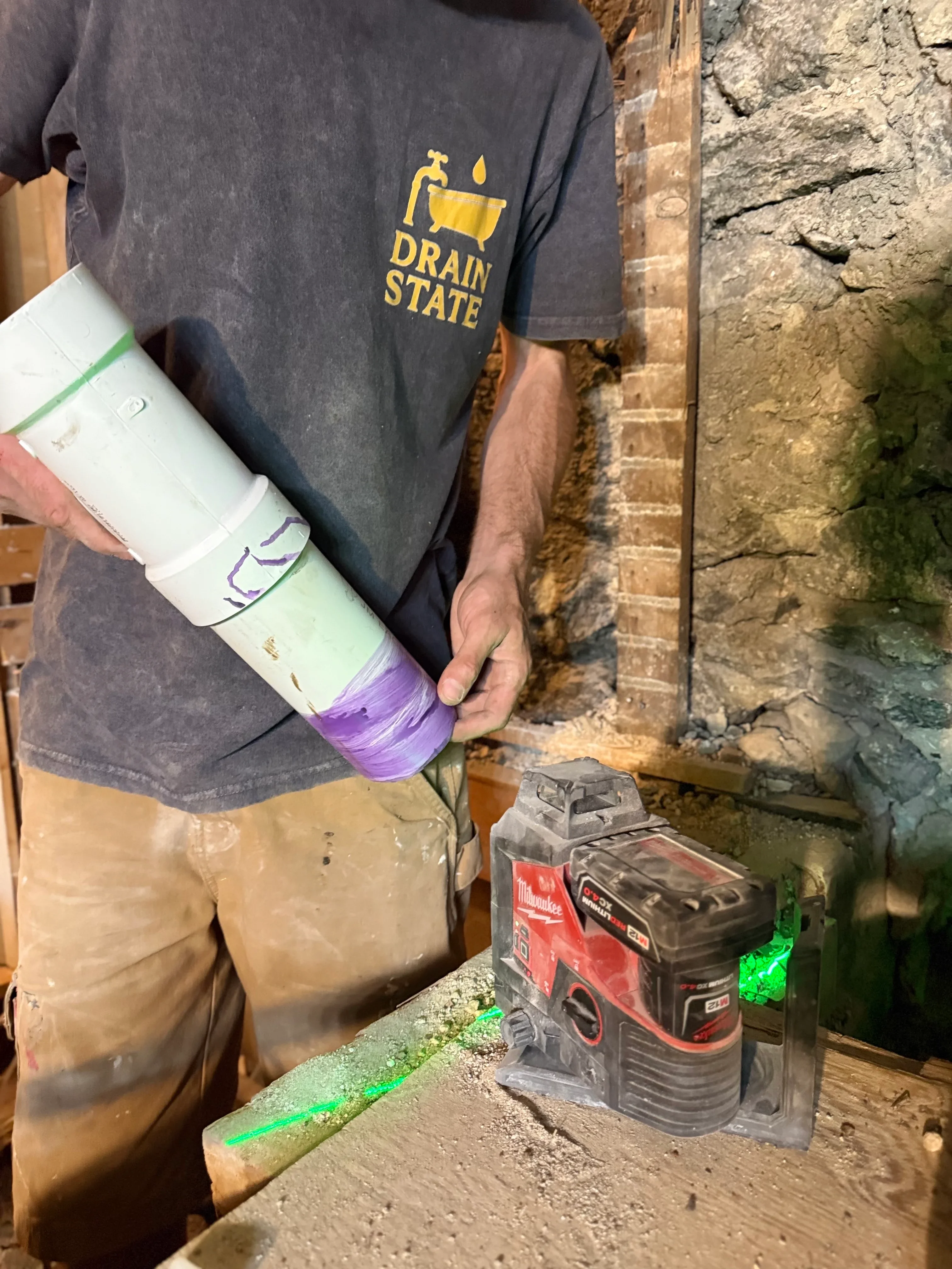 Plumber holding diagnostic drain inspection equipment against stone foundation wall