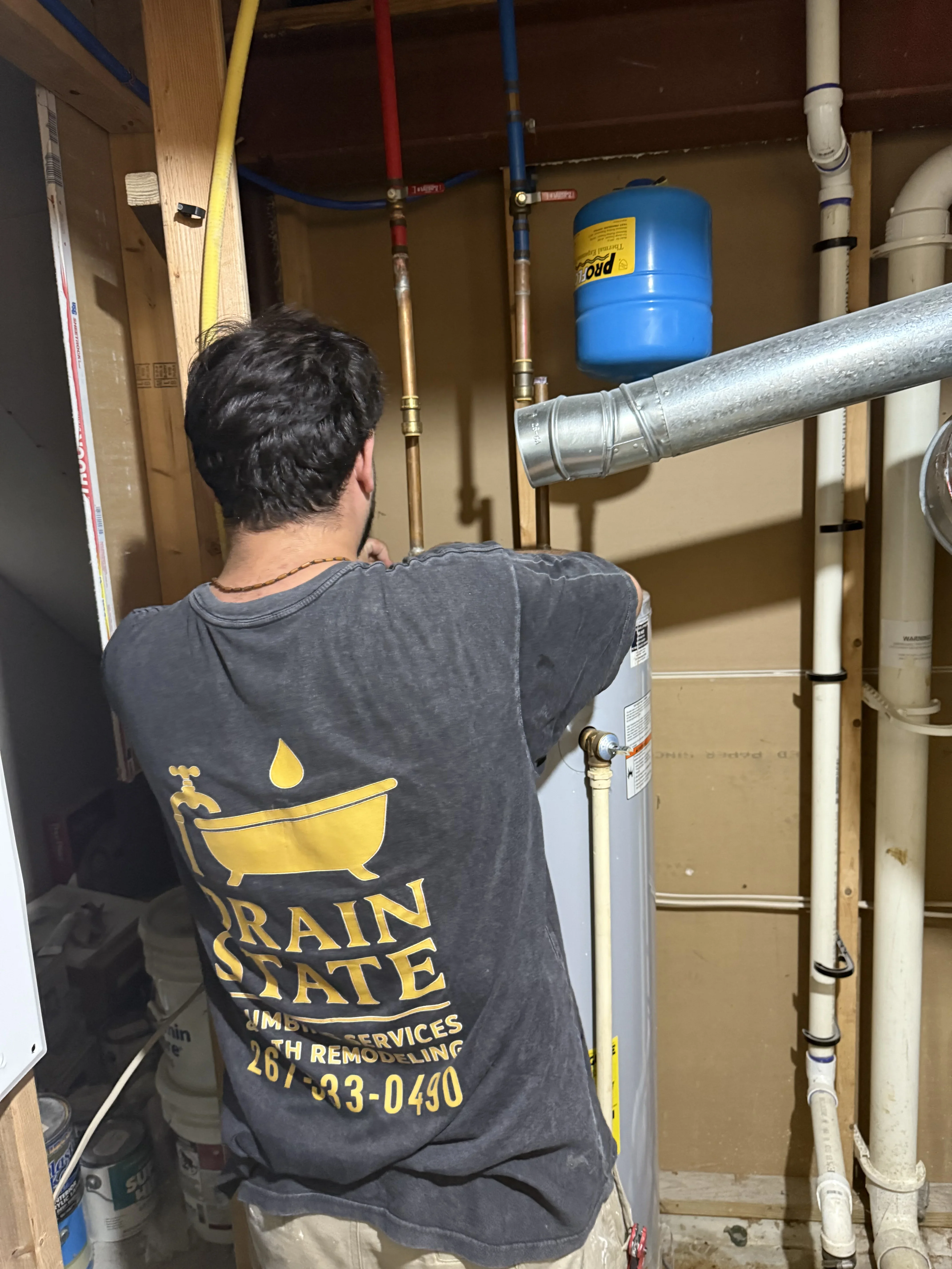 Plumber installing water heater with copper piping, expansion tank, and color-coded supply lines